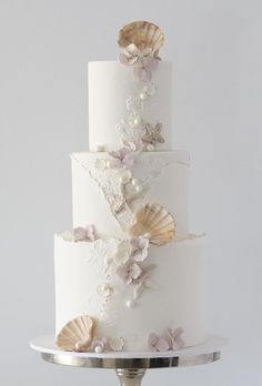 a three tiered white wedding cake with seashells and flowers on the side