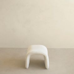 a small white stool sitting on top of a cement floor next to a beige wall