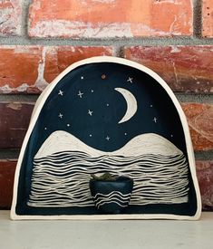 an artistic wooden sculpture with a night sky and stars on the moon over water in front of a brick wall