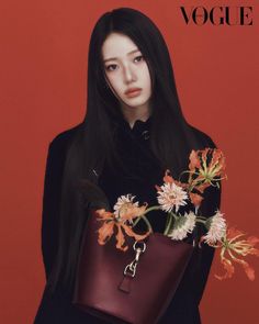 a woman with long black hair holding a brown bag and flowers in her hand, against a red background