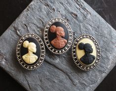 Beautiful African cameos set in detailed antique silver. Cameos feature a detailed African woman with broad shoulders, earrings and a necklace adorning her neck. Choose from cream and black, brown and black or black and cream cameos. Details: *Measures approx 28mm x 18mm *Secure pin back *Cameo is made of a hard, matte resin *Setting is plated brass *Back is lightly textured *Lightweight *Please note these brooches are significantly smaller than my regular size brooches, this size difference can Elegant Black Cameo Brooches, Cabochon Brooches As A Gift, Victorian Style Brooches For Gift, Kwanzaa Gifts, Green Brooch, Cameo Jewelry, Kwanzaa, Cameo Brooch, Silver Lockets