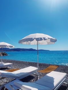 lounge chairs and umbrellas on the beach with clear blue water in the back ground