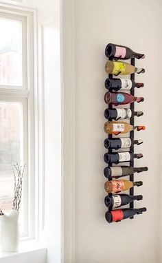 a wall mounted wine rack filled with lots of bottles next to a window in a white room