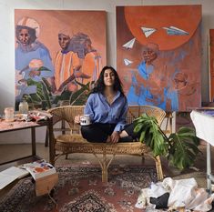 a woman is sitting on a wicker chair in front of some paintings and plants