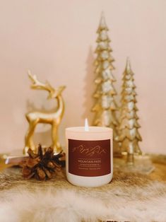 a white candle sitting on top of a table next to a gold statue and christmas trees