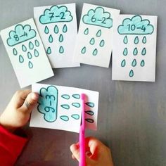 a person holding a pink pen in front of four cards with rain drawings on them