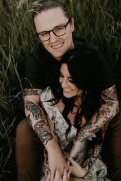 a man and woman sitting next to each other in the grass with tattoos on their arms