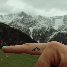 a person's hand with a small mountain tattoo on the middle finger, in front of snow - capped mountains