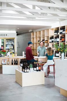 two men and a woman standing at a counter with wine bottles