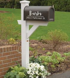 a black mailbox sitting on top of a white post in front of a brick wall