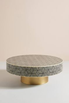 a round coffee table with a black and white pattern on the top, against a pink wall