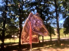 a close up of a glass horse head on a stick in the grass near trees