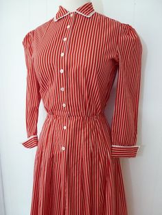 Amazing vintage 70's shirt dress by Adele Simpson!!Features include:Red and white stripe dress with nipped waistlineWhite eyelet trim at cuffs and collarButtons up front from neckline to mid hip lengthCute folded cuffsAdele Simpson label insideEra:1970'sMeasurements:Shoulder to shoulder - 14"Around chest, underneath armpits - 35"Across waist - 24""Across hips - 42"Top of shoulder to bottom hem - 45"I'd say this would best fit a size S or XS, but please consult measurements for an accurate fit!Al Striped Fitted Cotton Shirt Dress, Fitted Striped Cotton Shirt Dress, Striped Cotton Shirt Dress With Buttons, Fitted Striped Shirt Dress For Daywear, Classic Striped Button-up Shirt Dress, Summer Button-up Dress With Striped Collar, Striped Fitted Collared Dress, Fitted Striped Shirt Dress With Buttons, Classic Striped Cotton Dress