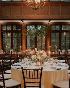 a table set up for a formal dinner with candles and flowers on the tables in front of large windows