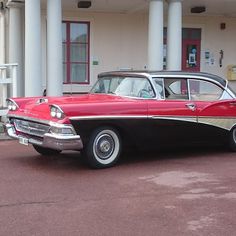 an old red and black car parked in front of a building