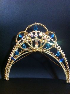 a gold tiara with blue and white stones on it's sides, against a black background