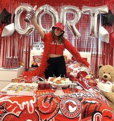 a woman standing in front of a bed with red decorations and balloons on the wall