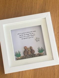 a white frame with some rocks and plants in it on top of a wooden table