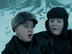 two young boys in winter clothes standing next to each other with snow on the mountain behind them