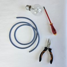 some tools are laying out on a white surface with one light bulb and two pliers