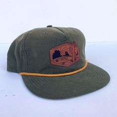 Need a new fun hat for all your day to day adventures?! We got you covered. This super comfy, lightweight five panel rope hat will be your best friend this summer. This design was created by Akinz owner and founder Suzanne Akin. Engraved faux-leather patch on an olive green 5-panel nylon hat with golden mustard yellow rope. Adjustable Curved Brim Hat For Camping, Adjustable Trucker Dad Hat With 5 Panels, Adjustable Trucker Dad Hat, Adjustable Flat Brim Baseball Cap For Camping, 5-panel Snapback Travel Hat, One Size Fits Most, Travel Snapback Hat, 5-panel, One Size, Adjustable Flat Brim Sun Hat For Hiking, 5-panel Snapback Hat For Travel, Adjustable Trucker Hat 5-panel