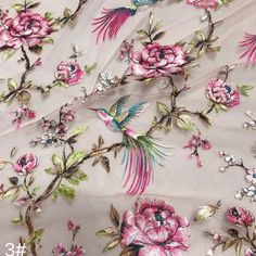 an embroidered fabric with pink flowers and birds on it, as well as green leaves