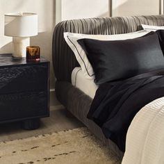 a bed with black and white sheets, pillows and a night stand next to it