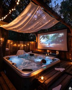 a hot tub in the middle of a wooden deck with string lights and a projection screen