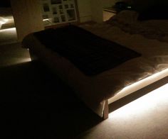 a bed that has some lights on it in the dark with its headboard turned down