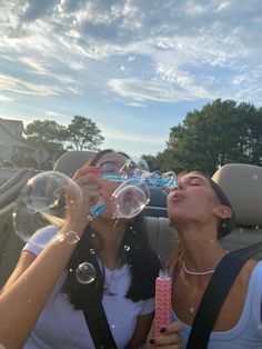 two women blowing bubbles in the back seat of a car