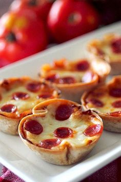 mini pizzas on a white plate with tomatoes in the backgroung behind them