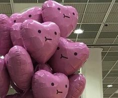 a bunch of pink heart shaped balloons hanging from the ceiling in an airport lobby, with faces drawn on them