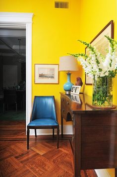 a blue chair sitting next to a wooden table in a room with yellow walls and wood floors