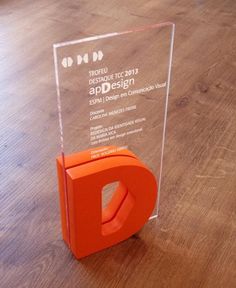 an orange plastic object sitting on top of a wooden floor next to a glass plaque