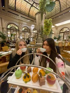 two women sitting at a table with plates of food in front of them and one holding a cup