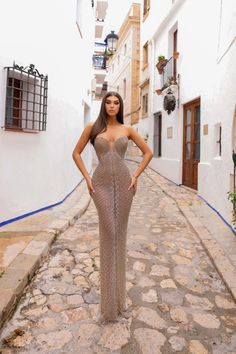 a woman is standing in an alley way wearing a long silver dress and posing for the camera with her hands on her hips