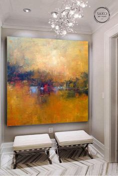 a large painting hanging on the wall above two stools in front of a chandelier