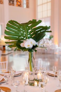 a vase filled with white flowers and greenery on top of a dining room table