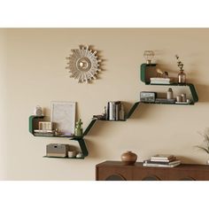 three green shelves on the wall with books and other items in them, one shelf has a sunburst hanging from it