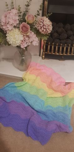 there is a crocheted rainbow blanket on the floor next to a vase with flowers