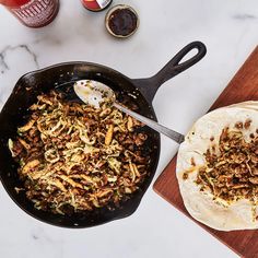 a skillet filled with food next to a tortilla on a cutting board