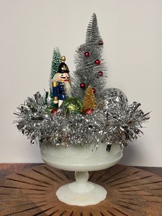 a white bowl filled with tinsel covered christmas trees and small toy figurines