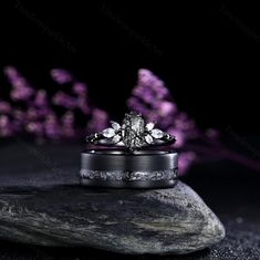 two wedding rings sitting on top of a rock with purple flowers in the back ground