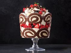 a cake with strawberries and cream on top is sitting on a glass pedestal in front of a black background