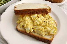 an egg salad sandwich on a white plate next to a bowl of broccoli