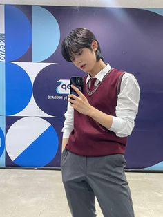 a young man wearing a maroon sweater vest and gray slacks is looking at his cell phone