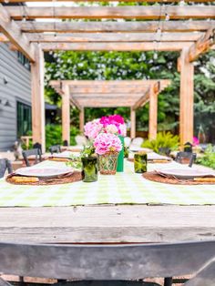 an outdoor dining table with flowers in vases and plates on the table, surrounded by greenery