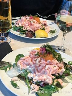 two white plates with food on them sitting on a table next to glasses of wine