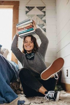 a woman is sitting on the floor with her feet in the air and holding books over her head