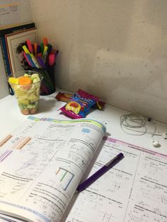 an open book sitting on top of a desk next to a cup of pencils